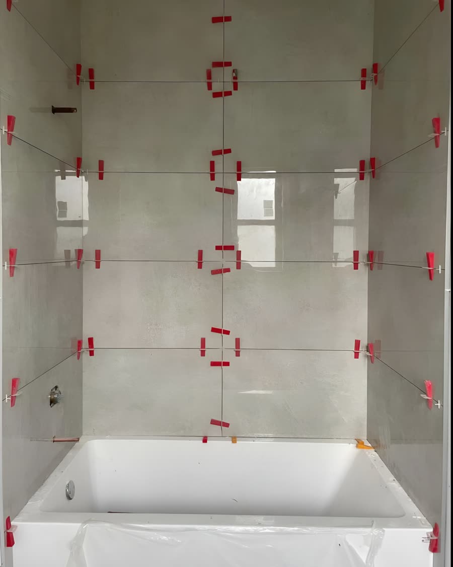 Large format shower tile set on a tub surround with levelling clips still in place.