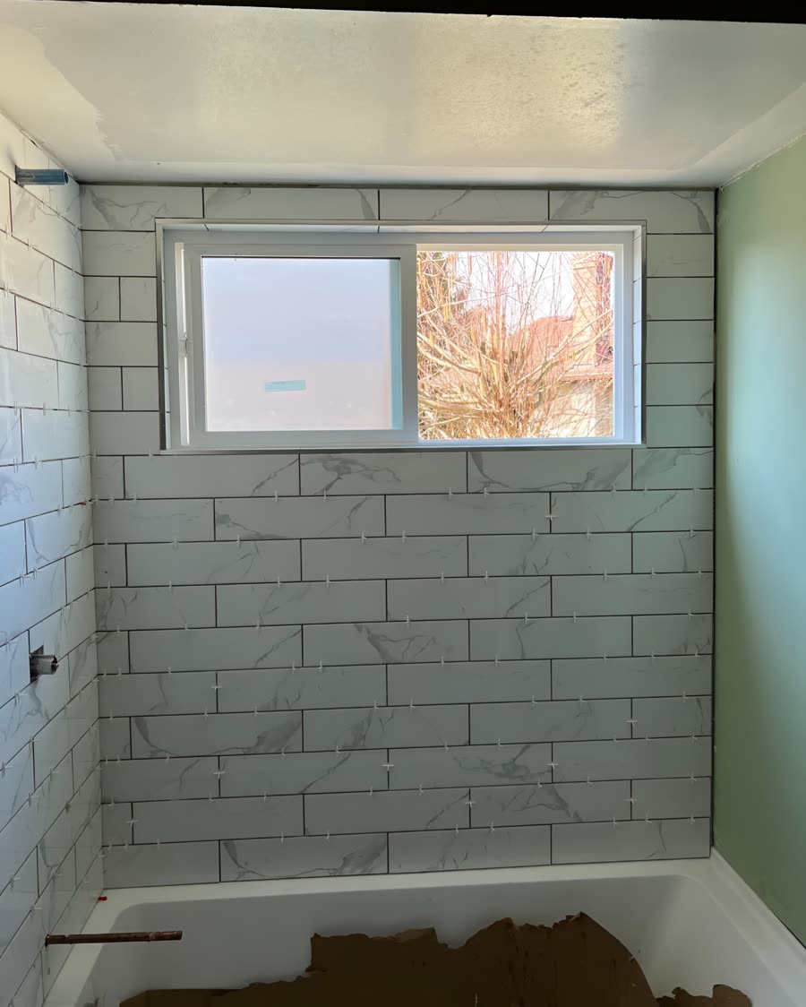 White marble effect subway tile running up a tub surround around a window.